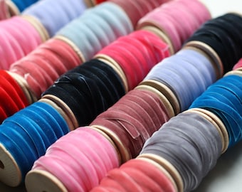 May include: A collection of spools of velvet ribbon in various colors, including red, blue, pink, black, gray, and purple. The ribbon is wound around wooden spools.