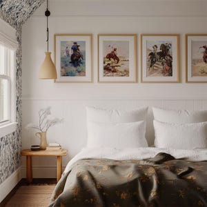 May include: A bedroom with a white bed with a green floral patterned blanket and white pillows. There are four framed pictures of cowboys on horseback on the wall above the bed. A wooden side table with a vase of flowers and a book sits next to the bed.