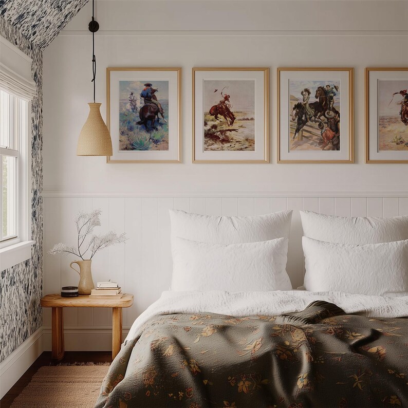 May include: A bedroom with a white bed with a green floral patterned blanket and white pillows. There are four framed pictures of cowboys on horseback on the wall above the bed. A wooden side table with a vase of flowers and a book sits next to the bed.