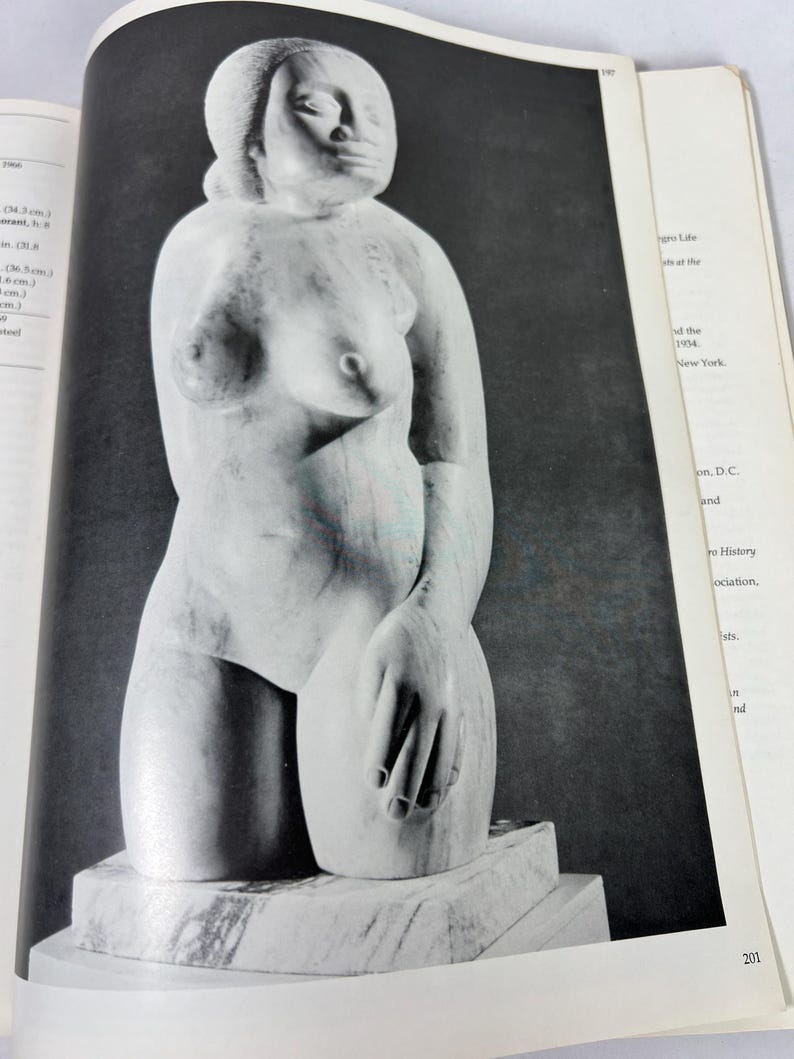 May include: A black and white photograph of a marble sculpture depicting a torso of a figure with a smooth, rounded head and defined facial features. The figure is shown from the waist up, resting on a rectangular marble base within a book page.
