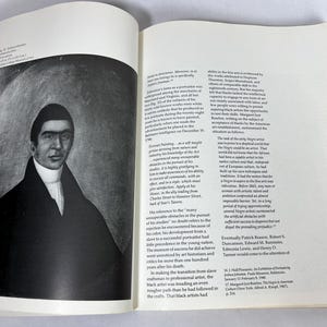 May include: An open book page featuring a black and white portrait of a man in a dark coat with a high collar, set against a circular background. The adjacent page contains printed text columns discussing the artist Joshua Johnson and his work.