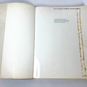 May include: An open book with off-white pages featuring the title Two Centuries of Black American Art at the top right. The text below states the exhibition was made possible by grants from the National Endowment for the Humanities and Philip Morris.