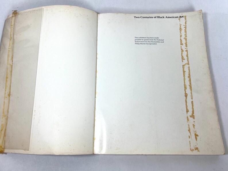 May include: An open book with off-white pages featuring the title Two Centuries of Black American Art at the top right. The text below states the exhibition was made possible by grants from the National Endowment for the Humanities and Philip Morris.
