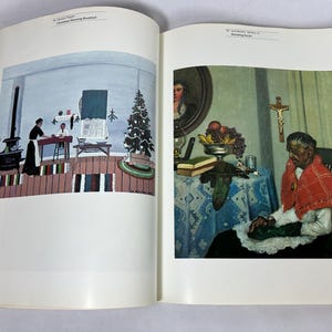 May include: An open art book displaying two distinct paintings on facing pages. The left page features 'Christmas Morning Breakfast' by Horace Pippin. The right page shows 'Mending Socks' by Archibald J. Motley Jr., depicting a person sewing.
