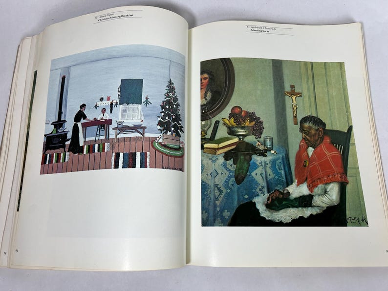 May include: An open art book displaying two distinct paintings on facing pages. The left page features 'Christmas Morning Breakfast' by Horace Pippin. The right page shows 'Mending Socks' by Archibald J. Motley Jr., depicting a person sewing.