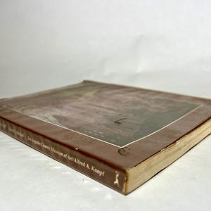 May include: A softcover book with a brown cover featuring a rectangular image on the front. The spine and cover display the text Los Angeles County Museum of Art and Alfred A. Knopf. The book is positioned at an angle, showing the front cover.