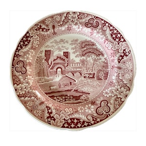 May include: A vintage pink and white ceramic plate with a detailed floral border and a central image of a bridge and buildings in a landscape.