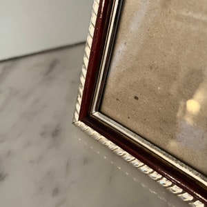Puede incluir: Primer plano de un marco de fotos rectangular con un borde plateado en forma de cuerda y un marco interior marr&oacute;n oscuro. El marco contiene una imagen de color claro y se encuentra sobre una superficie de m&aacute;rmol blanco.