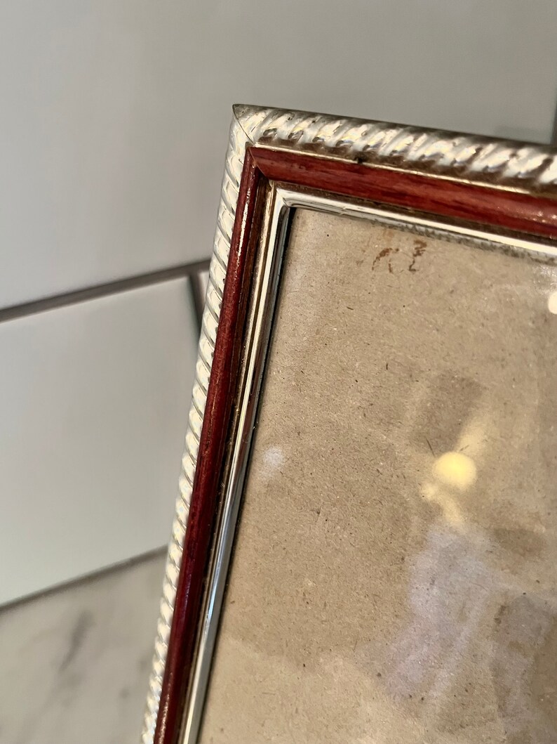 Puede incluir: Primer plano de un marco de fotos rectangular con un borde plateado y blanco en forma de cuerda. El marco tiene un borde interior rojo oscuro y un borde interior plateado. El marco est&aacute; en &aacute;ngulo, mostrando un vistazo de la foto en el interior.
