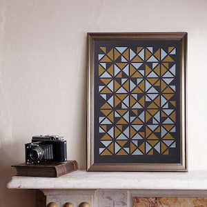 May include: A framed print with a geometric pattern of gold and light blue triangles on a black background. The frame is silver with a dark wood finish.