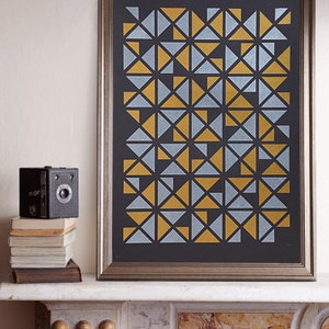 May include: A framed print featuring a geometric pattern of gold and silver triangles on a black background.