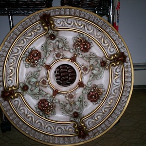 May include: A decorative ceiling medallion with a white background and gold and brown accents. The medallion features a floral design with intricate details.