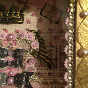 May include: A pink and gold shadow box with a crown, wings, and ribbons. The box is decorated with pink flowers and pearls. The text "10 things I will never forget" is visible in the box.