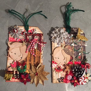 May include: Two Christmas-themed gift tags with a girl illustration, snowflakes, a sled, and other festive embellishments. The tags are decorated with red, gold, and green accents.