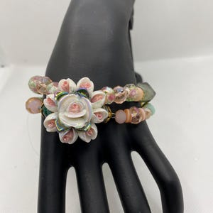 May include: A multi-strand bracelet with pink, white, and green beads. The bracelet features a large white flower charm with pink accents.