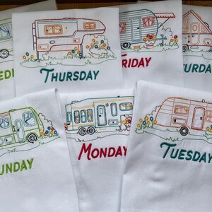 May include: White kitchen towels embroidered with colorful camper designs, each labeled with a day of the week. The embroidery features detailed outlines of RVs with floral accents, perfect for a camping or travel theme.