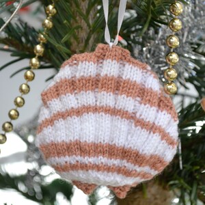 May include: A knitted Christmas bauble shaped like a seashell with brown and white stripes hanging on a Christmas tree.