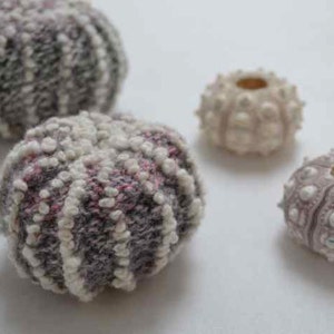 May include: Four sea urchins, two are gray and white with a textured surface, one is white with a smooth surface, and one is purple with a smooth surface.