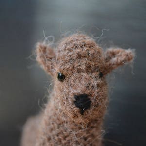 May include: Close-up of a brown and white knitted llama toy with a black nose and brown eyes.