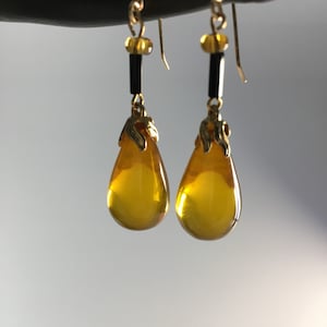 May include: A pair of gold tone dangle earrings with teardrop shaped amber glass beads. The earrings have black beads and gold accents.