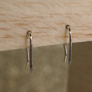 May include: A pair of silver hoop earrings with a simple, minimalist design. The earrings are small and delicate, and they are perfect for everyday wear.
