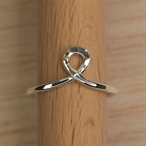 May include: A silver ring with a simple, twisted design. The ring is shown on a wooden surface.