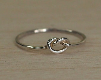 May include: A silver knot ring with a simple design. The ring is made of a thin band of metal and has a knot in the center.