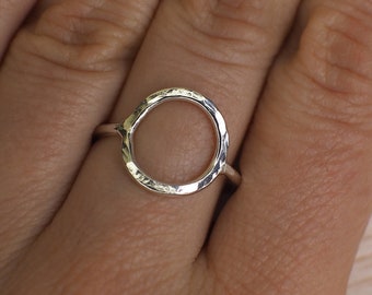 May include: A silver ring with a hammered, circular design. The ring is worn on a finger.