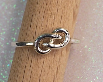 May include: A silver ring with a knot design. The knot is a simple, continuous loop.