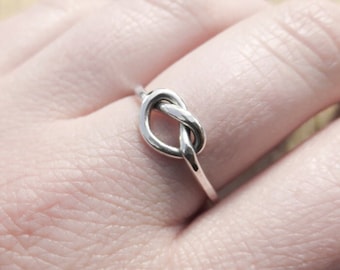 May include: A silver knot ring with a simple design. The ring is worn on a finger.
