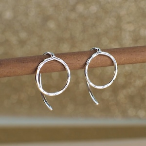 Two sterling silver circle earrings with a hammered texture. The earrings are displayed on a brown wooden surface and have curved hook backs.