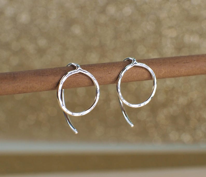 Two sterling silver circle earrings with a hammered texture. The earrings are displayed on a brown wooden surface and have curved hook backs.
