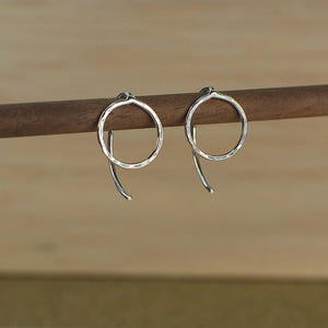 Two minimalist sterling silver circle earrings with a hammered textured surface. The earrings are hanging from a wooden surface and catch the light.
