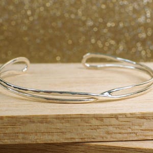 May include: A silver double-strand bangle bracelet with a hammered finish. The bracelet is open and has a simple, elegant design.