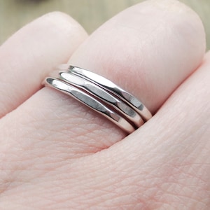 May include: Three silver hammered stacking rings worn on a finger.