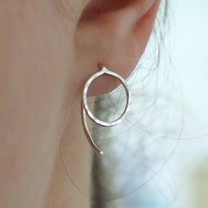 A sterling silver circle earring with a curved hook back. The hoop shaped earring has a polished hammered surface to catch the light. Shown in an earlobe.