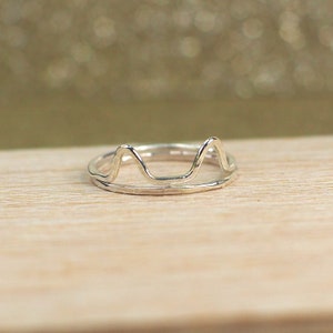 May include: A silver ring with a wavy, mountain-like design. The ring is simple and delicate.