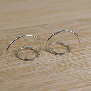 Two silver hoop earrings with a circular design. Each earring is a single hoop that is bent into a curve with a hammered circle on the front.