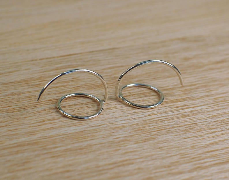 Two silver hoop earrings with a circular design. Each earring is a single hoop that is bent into a curve with a hammered circle on the front.