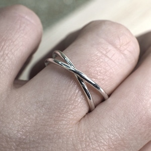 May include: A silver ring with two bands that cross over each other. The ring is worn on a finger.