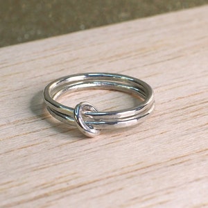 May include: A silver ring with a knot design. The ring is made of two bands that are intertwined.