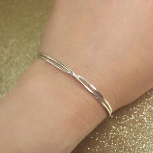 May include: A silver bangle bracelet with a simple, elegant design. The bracelet is made of two thin bands of metal that are twisted together.