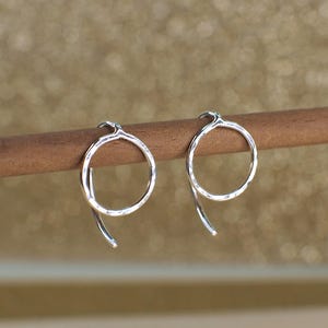 Two sterling silver circle jacket earrings with a hammered texture. The earrings are hanging from a wooden surface.