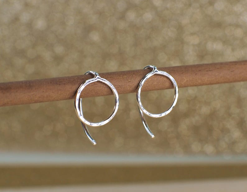 Two sterling silver circle jacket earrings with a hammered texture. The earrings are hanging from a wooden surface.