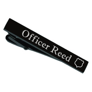 May include: Black tie bar with the text "Officer Reed" engraved in white lettering and a small shield design.