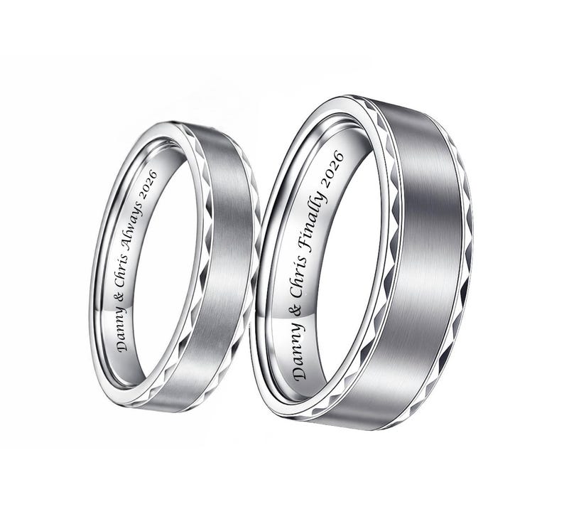 May include: Two silver wedding bands with engraved text. One ring reads "Danny & Chris Always 2026" and the other reads "Danny & Chris Finally 2026". The rings have a brushed metal finish with a geometric design around the edges.