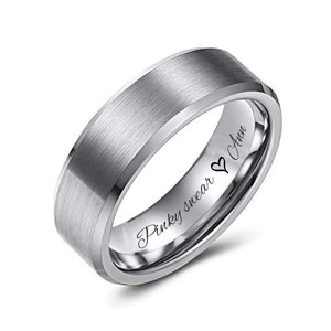 May include: A silver-colored ring with a brushed metal finish. The ring has a flat top and beveled edges. The inside of the ring is engraved with the words "Pinky swear" and "Ann" with a heart symbol. A close-up shot against a white background.