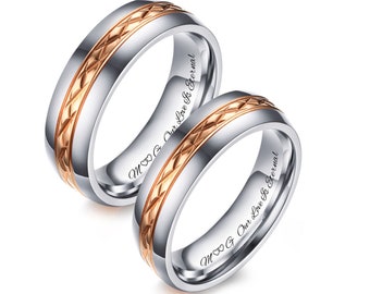 Könnte beinhalten: Zwei silberne Ringe mit einem roségoldenen Mittelband mit Rautenmuster. Die Ringe tragen die Inschrift "M & G Our Love Is Eternal". Die Ringe sind vor weißem Hintergrund abgebildet.