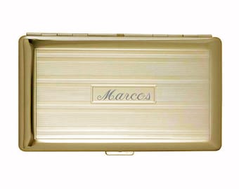 May include: A gold metal cigarette case with a horizontal ribbed design and the name "Marcos" engraved on the front.