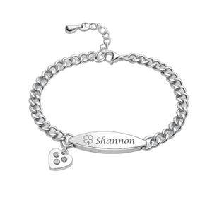 May include: Silver-toned bracelet with a curb chain design. The bracelet features an oval charm engraved with the name "Shannon" and a clover symbol. A small heart charm with three embedded clear stones dangles from the bracelet.